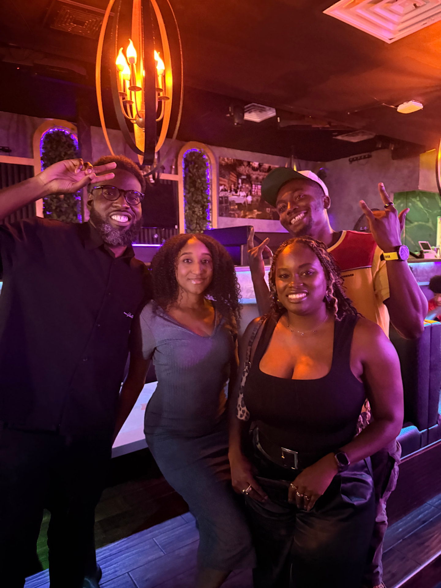 Four friends throwing peace signs under purple lounge lights